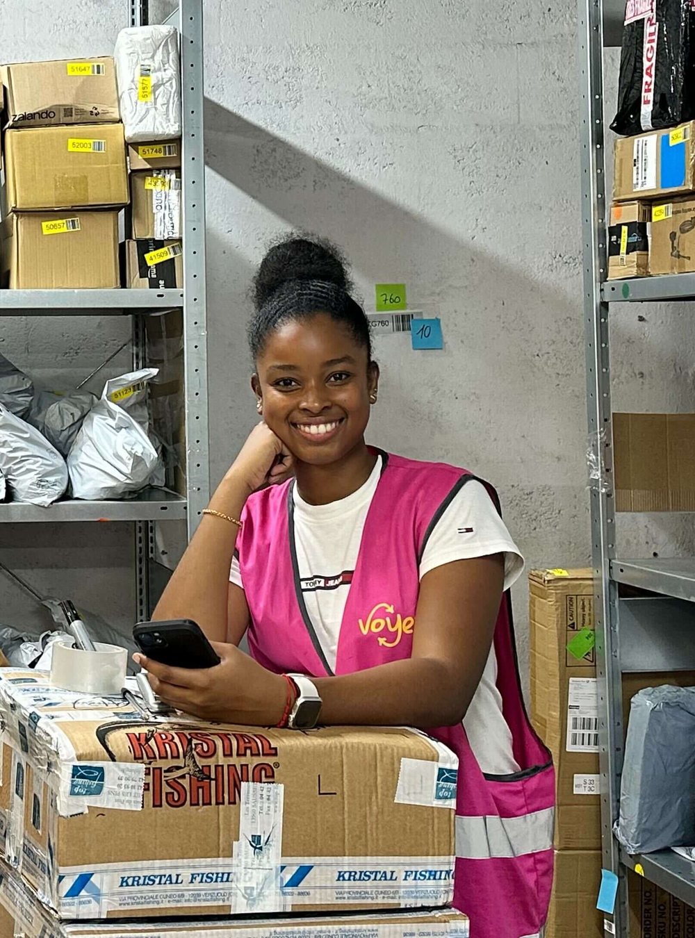 Une conseillère Voyey souriante devant les étagères de colis prêts au retrait